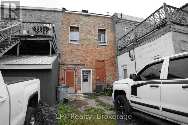 Rear view of a brick building with two doors, a trash can, and pickup trucks parked outside. - 551 Turnberry Street, Huron East