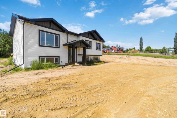Angled exterior view of the white house with dark trim, featuring a large window and rural landscape. - #401 55108 Range Road 15, Rural Lac Ste  Anne County