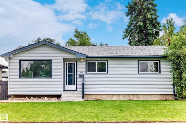 Front view of a light blue vinyl-sided bungalow with a large bay window and a concrete walkway. - 5519 142 Av Nw Nw, Edmonton
