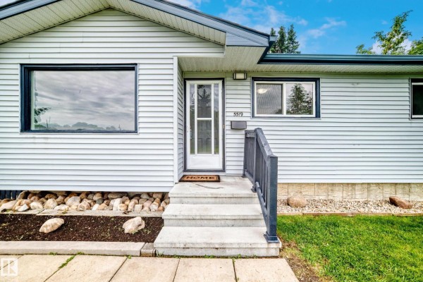 Close-up exterior view of a light blue vinyl-sided bungalow entrance with concrete steps and a welcome mat. - 5519 142 Av Nw Nw, Edmonton