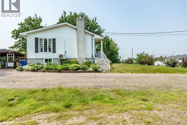 Side view of a white house with white siding, a prominent brick chimney, and garden beds. - 5519 Route 117, Baie Sainte Anne