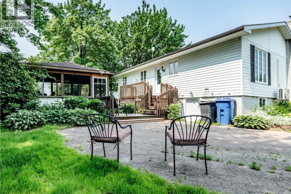 Backyard patio with two chairs, a wooden deck, screened-in gazebo, and white house exterior. - 5519 Route 117, Baie Sainte Anne