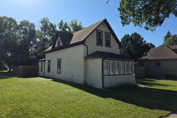 Side view of a house with a wooden fence and green lawn. - 552 1st Street Nw, Portage La Prairie