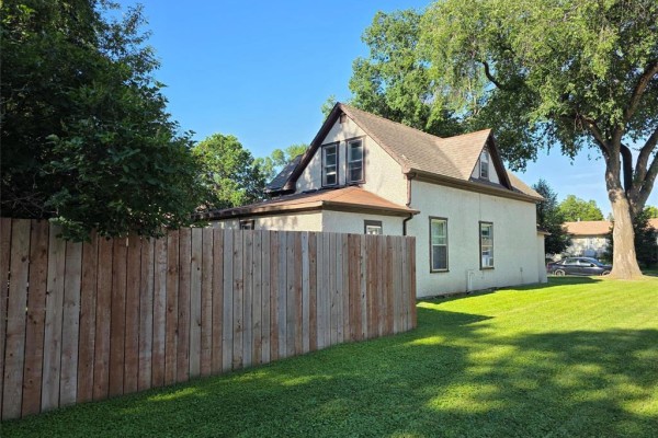 Backyard view of the house, showing a wooden fence and mature trees. - 552 1st Street Nw, Portage La Prairie