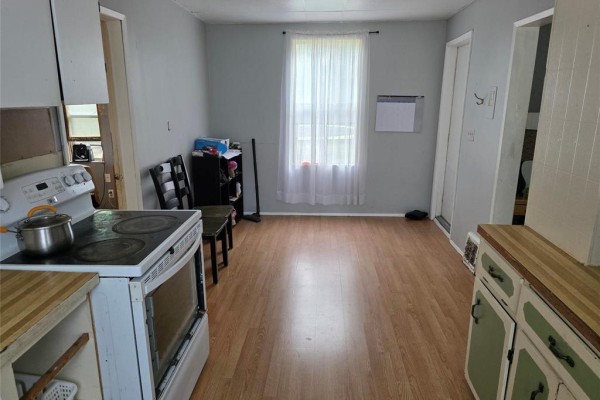 View of a kitchen with a stove, cabinets, and a window with sheer curtains. - 552 1st Street Nw, Portage La Prairie