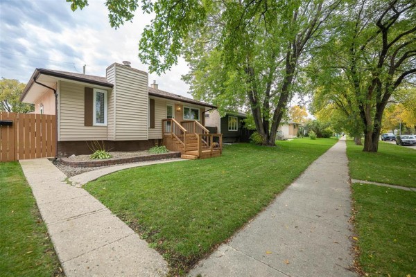 Side view of the house showing a wooden porch, steps, and a concrete sidewalk on a green lawn. - 552 Ravelston Avenue W, Winnipeg