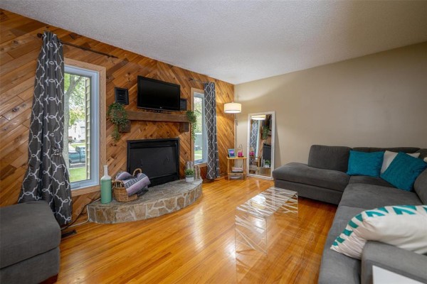 Living room with hardwood floors, a stone fireplace with a television above, and a grey sectional sofa. - 552 Ravelston Avenue W, Winnipeg