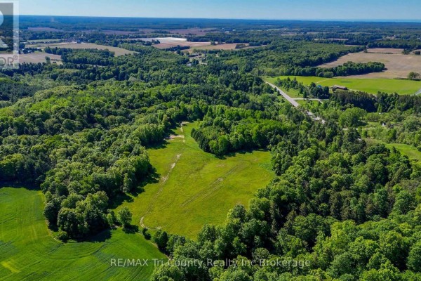 Aerial view of a cleared grassy field within a forest, under a blue sky. - 55234 Heritage Line, Bayham
