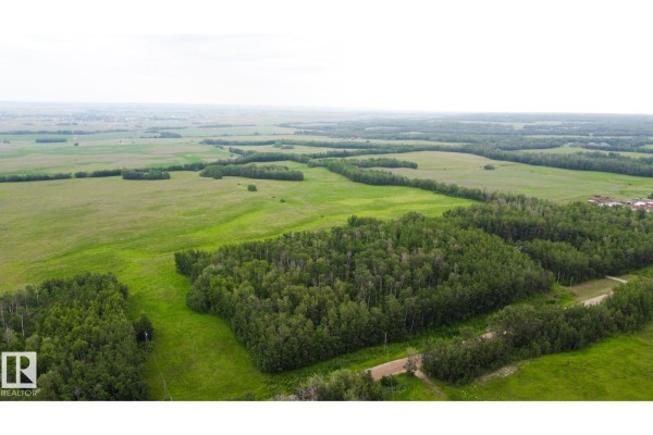 Aerial view of a large, flat, green lot with scattered trees and distant fields under a cloudy sky. - 553-lot B Range Road 201, Rural Lamont County