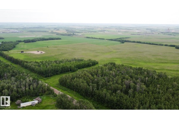 Aerial view of a rural landscape featuring a treed area, a mobile home, and distant agricultural fields. - 553-lot C Range Road 201, Rural Lamont County