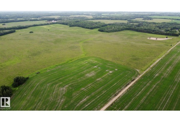 Wide aerial perspective of undeveloped land with agricultural fields, trees, and infrastructure in the distance. - 553-lot D Range Road 201, Rural Lamont County