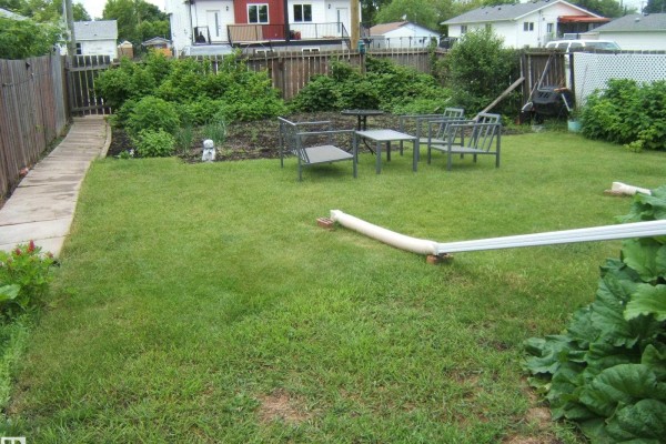 Backyard view with a green lawn, outdoor furniture, wooden fence, and detached garage. - 5530 50 St, Vegreville
