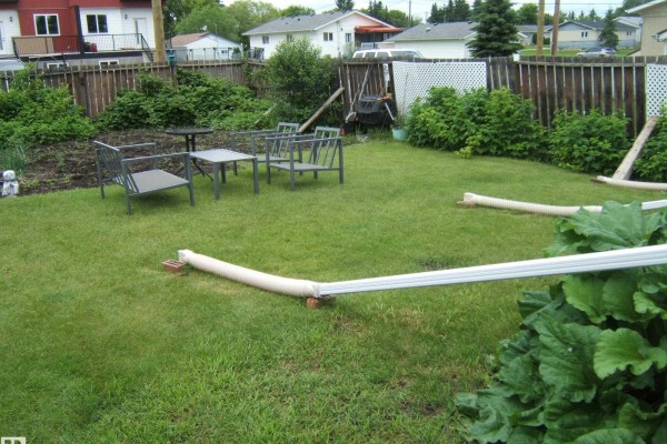 Green lawn with outdoor seating, a patio table, and drainage pipes extending into the grass. - 5530 50 St, Vegreville