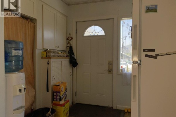Interior view of a doorway with a white door, water cooler, stacked boxes, and a white refrigerator. - 555 Carson Road, Grand Forks