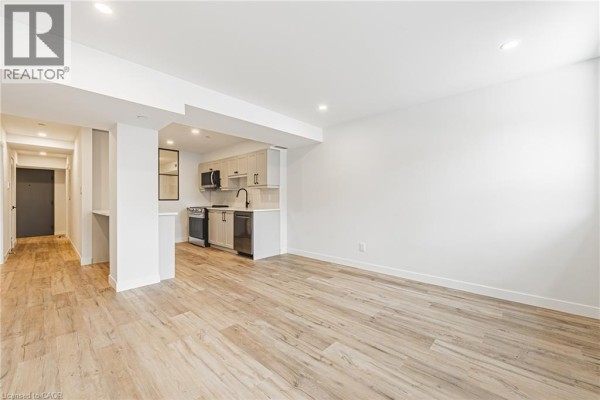 Living area with view of small kitchen and hallway, featuring light wood floors. - 555 Sanatorium Road Unit# 102, Hamilton