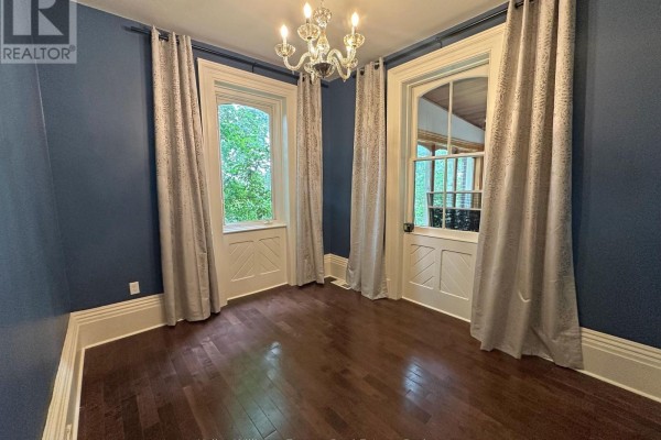 Room with dark blue walls, dark hardwood floors, and two tall windows with patterned drapes. - 555 Thornton Road S, Oshawa