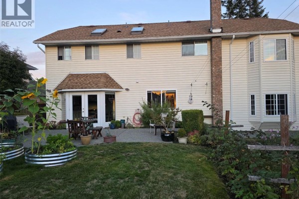 Backyard patio area with garden planters, patio furniture, and a grassy lawn. - 5550 Cherry Creek Rd, Port Alberni