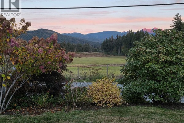 View of a rural landscape with hills, trees, and a pasture at sunset. - 5550 Cherry Creek Rd, Port Alberni