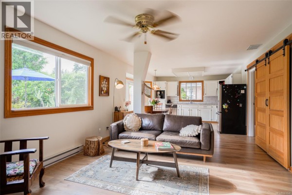 Living room with a brown leather sofa, coffee table, wood floors, and a view of the kitchen. - 5550 Cherry Creek Rd, Port Alberni