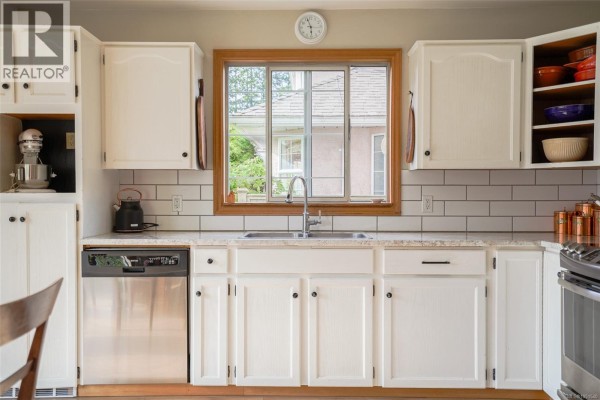 Kitchen with white cabinets, subway tile backsplash, stainless steel dishwasher, and a sink below a window. - 5550 Cherry Creek Rd, Port Alberni