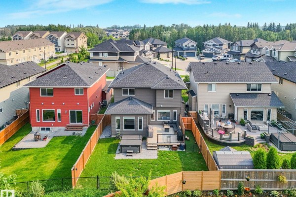 Rear view of a grey house with a wooden deck, hot tub, and fenced green backyard. - 556 Merlin Ld Nw, Edmonton