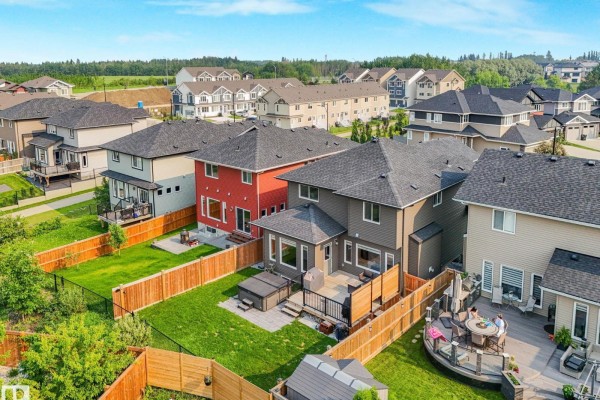 Aerial view of the backyard of a grey house with a wooden deck and adjacent red and tan houses. - 556 Merlin Ld Nw, Edmonton