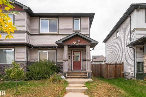Front view of a grey duplex with brown accents, a red door, and a covered porch. - 556 Secord Bv Nw, Edmonton