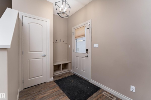 Entryway with a white door, bench with cubbies, and coat hooks against a tan wall. - 556 Secord Bv Nw, Edmonton