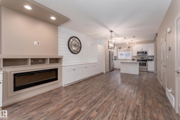 Open-concept living room with a fireplace, built-in cabinets, and a kitchen with an island. - 556 Secord Bv Nw, Edmonton