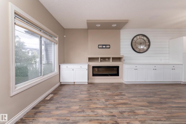 Living room with a large window, fireplace, and white cabinets overlooking the open kitchen. - 556 Secord Bv Nw, Edmonton