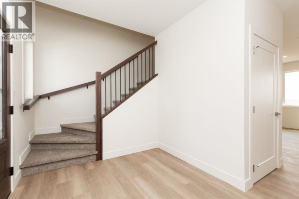 Hallway with a staircase, light wood-look flooring, and a white double door. - 558 Malahat Green W, Lethbridge