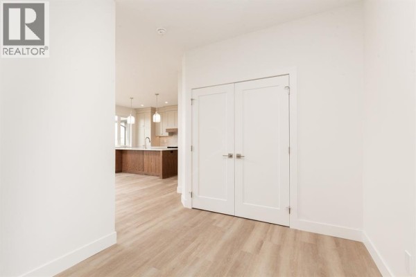 Hallway with white doors leading to a kitchen and dining area visible in the background. - 558 Malahat Green W, Lethbridge