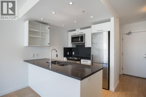 Kitchen with white cabinets, stainless steel appliances, and a dark countertop island with a sink. - 559 955 E Hastings Street, Vancouver