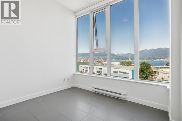 Empty room with grey tiled floors and large windows offering panoramic views of the city and water. - 559 955 E Hastings Street, Vancouver
