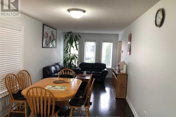 Dining room with wooden table and chairs, adjacent to living area with sofas. - 5590 Loonlake Avenue, Mississauga
