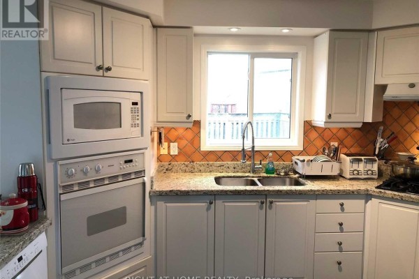 Kitchen with white cabinets, granite countertops, stainless steel double sink, and tiled backsplash. - 5590 Loonlake Avenue, Mississauga