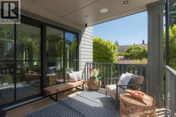 Covered balcony with seating area, patterned rug, metal railings, and views of trees and houses. - 5593 Mackenzie Street, Vancouver