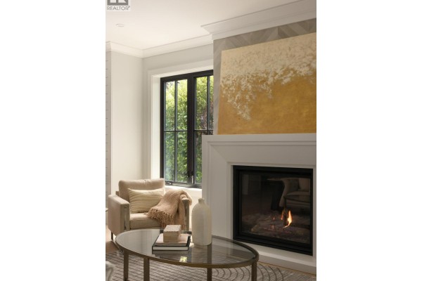 Close-up of a living room fireplace with a white mantel, marble surround, and adjacent armchair with a blanket. - 5593 Mackenzie Street, Vancouver
