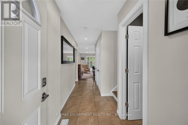 Interior hallway of townhouse looking towards living area with beige walls and tiled floor. - 56 - 30 Regent Avenue, Hamilton