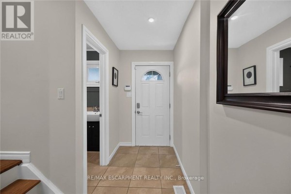 Interior hallway looking towards the front entrance with beige walls, tiled floor, and staircase. - 56 - 30 Regent Avenue, Hamilton