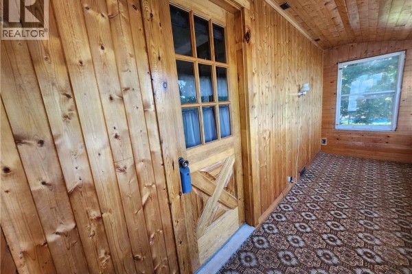 Living room with wood-look vinyl flooring, a brick fireplace surround, an arched doorway, and a wooden door. - 56 Airport Street, Dieppe