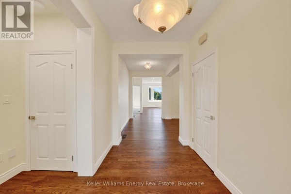 Wide hallway with dark hardwood floors and white doors leading into rooms. - 56 Elmdale Drive, Prince Edward County