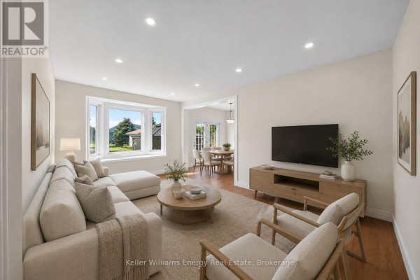 Living room with a sectional sofa, armchair, coffee table, and television. - 56 Elmdale Drive, Prince Edward County