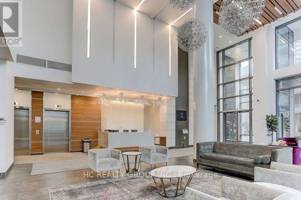 Spacious condo lobby with seating area, elevators, and contemporary chandelier lighting. - 56 Forest Manor Road, Toronto