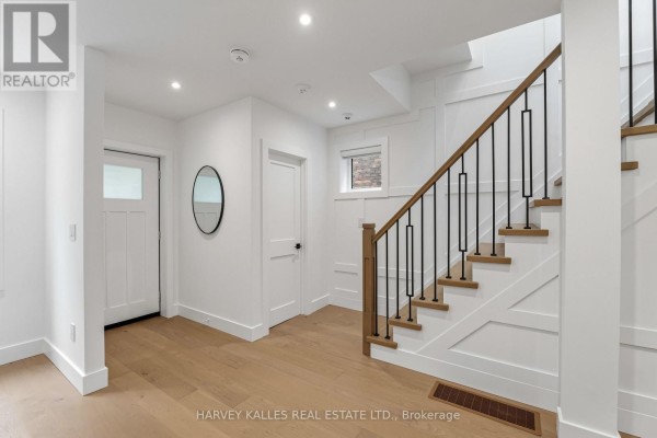Interior entryway with white walls, wood flooring, and a modern staircase with black railings. - 56 Glengarry Avenue, Toronto