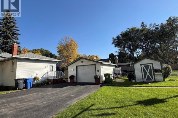 Side view of the white siding house with a chimney and autumn foliage. - 56 Haultain Avenue, Yorkton