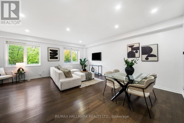 Living and dining area with dark hardwood floors, white sectional sofa, glass dining table with chairs, and large windows. - 56 Heron Park Place, Toronto