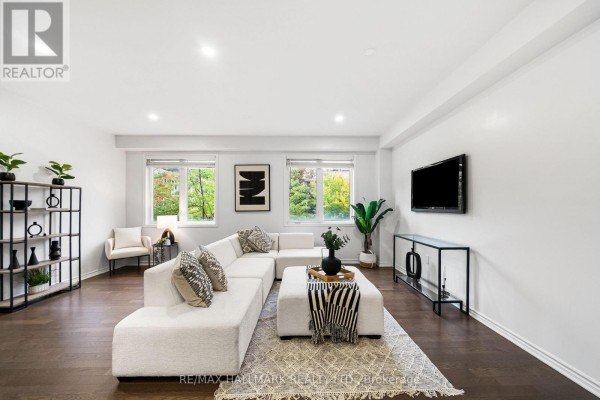 Spacious living room with a large white sectional sofa, ottoman, dining area, and windows overlooking trees and houses. - 56 Heron Park Place, Toronto