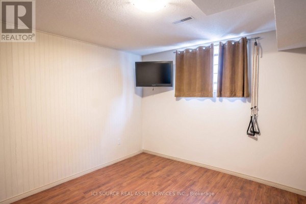 Basement room with white paneled walls, wood laminate flooring, and a wall-mounted television. - 56 Hersey Crescent, Barrie