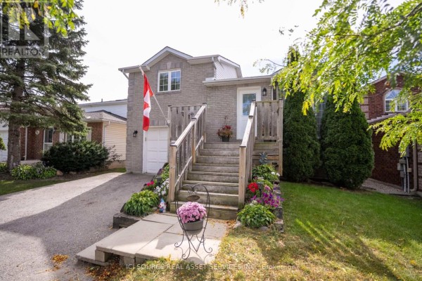Front exterior of a beige brick house with a Canadian flag and blooming flower beds. - 56 Hersey Crescent, Barrie